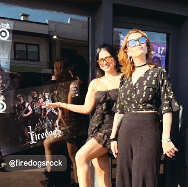 Público posando ao lado do cartaz da Firedogs